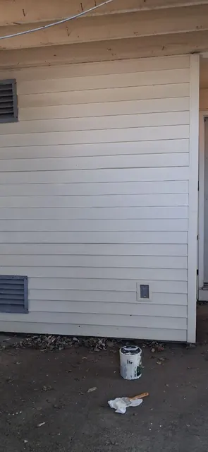 The same wall after painting: siding and trim in one even light color, with the paint can still at ground level.