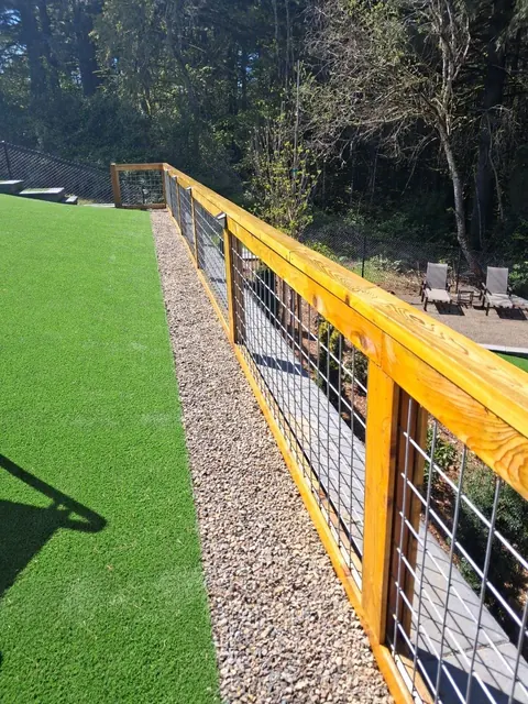 Warm-toned wood rails frame wire panels beside a green lawn and gravel border.