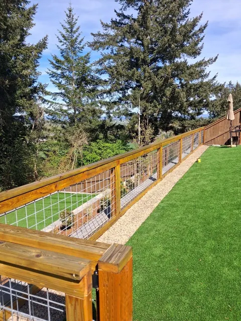 Wood-and-wire fence panels follow the edge of a sloping lawn, with a gravel strip along the base.