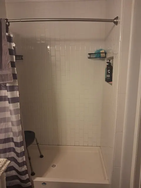 Before the remodel: the original white tile enclosure with a curtain rail, corner baskets and a recessed niche.