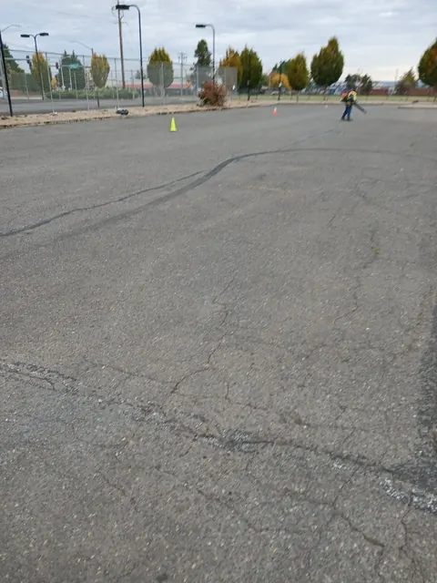 Worn, cracked asphalt with no visible parking bays. Cones are set out and the lot is being cleared.