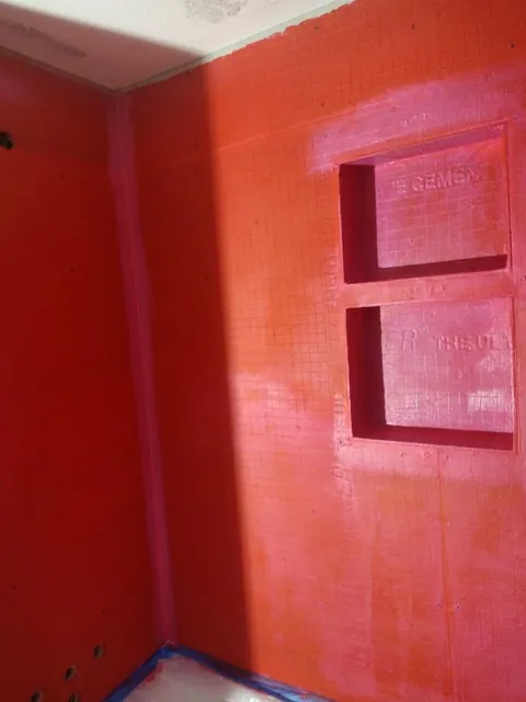 Red-coated wall boards and two recessed niches are visible before the tile goes on; the tub below is protected.